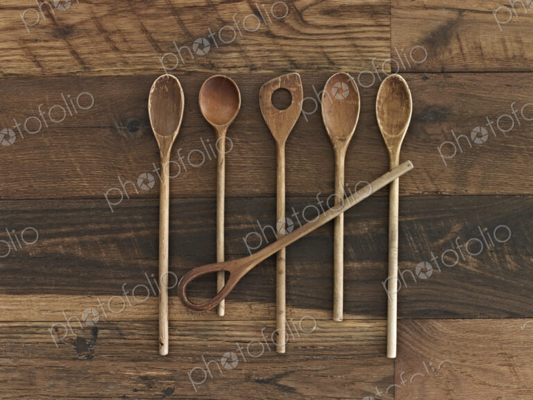 An arrangement of six wooden spoons of a variety of shapes and sizes on a wooden table.