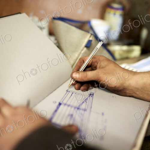 An artisan metal worker drawing up designs for a gate in a sketchbook An artisan metal worker drawing up designs for a gate in a sketchbook