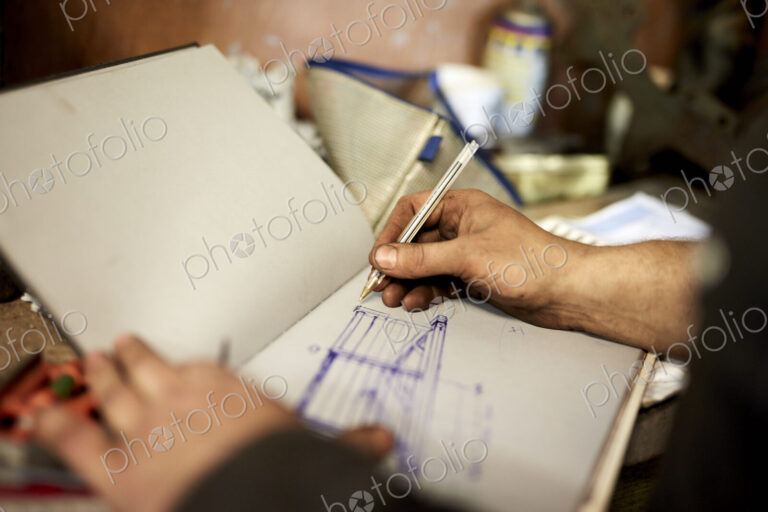 An artisan metal worker drawing up designs for a gate in a sketchbook