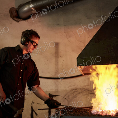 An artisan metal worker heating metal in a forge in his workshop. An artisan metal worker heating metal in a forge in his workshop.