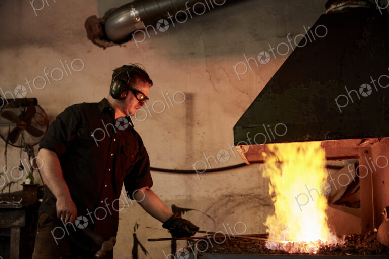 An artisan metal worker heating metal in a forge in his workshop.