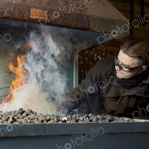 An artisan metal worker heating metal in a furnace fire. An artisan metal worker heating metal in a furnace fire.
