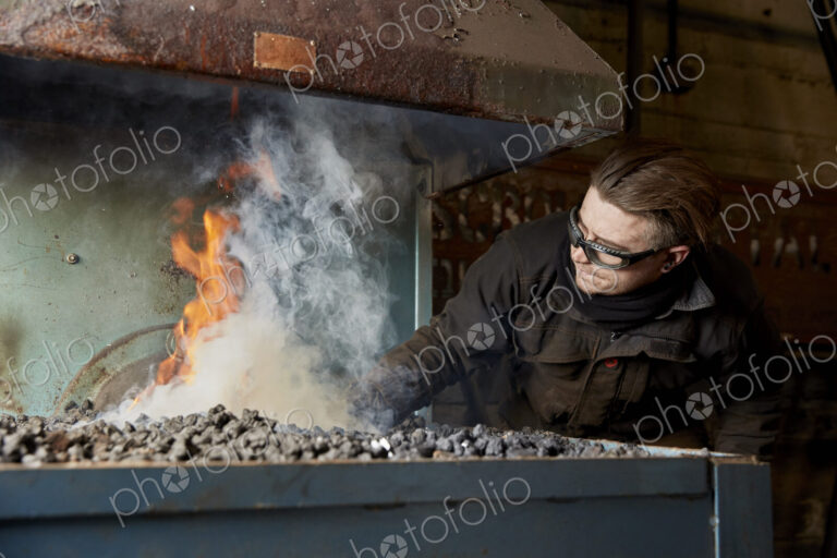 An artisan metal worker heating metal in a furnace fire.