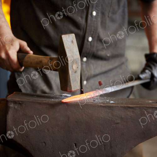 An artisan metal worker shaping a red hot piece of metal on an anvil.