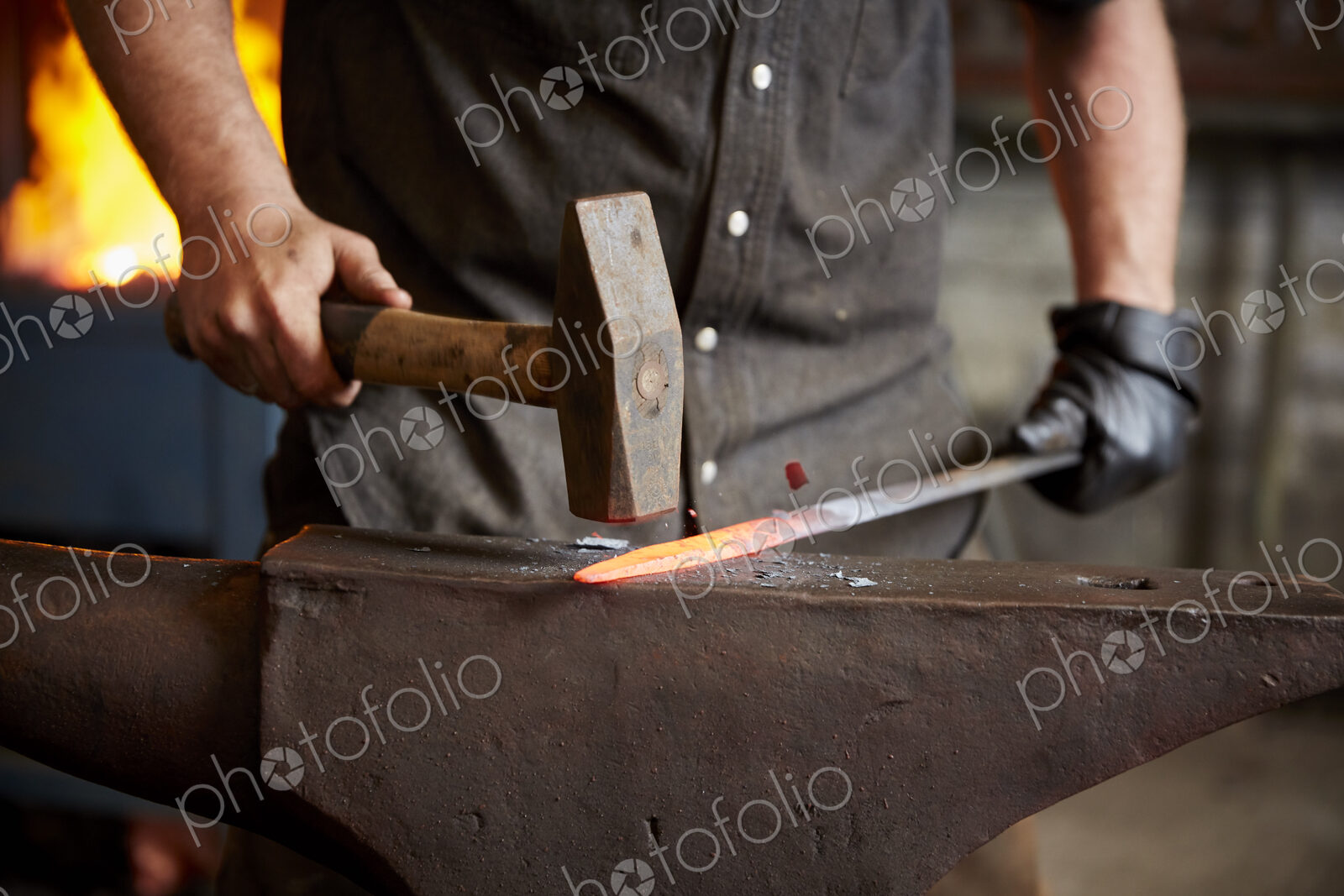 An artisan metal worker shaping a red hot piece of metal on an anvil.