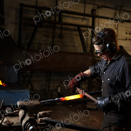 An artisan metal worker using hammer and anvil to shape a red hot glowing piece of metal An artisan metal worker using hammer and anvil to shape a red hot glowing piece of metal