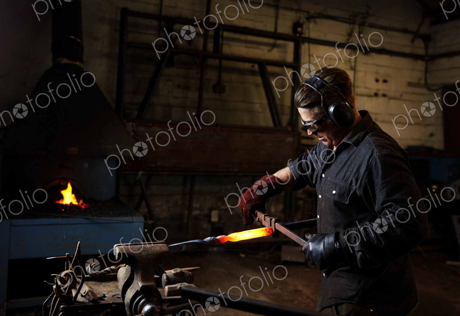 An artisan metal worker using hammer and anvil to shape a red hot glowing piece of metal