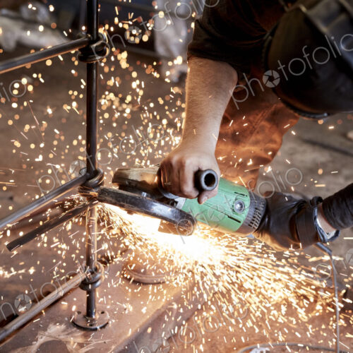 An artisan metalworker at work holding an angle grinder, workng on a metal fence. An artisan metalworker at work holding an angle grinder, workng on a metal fence.