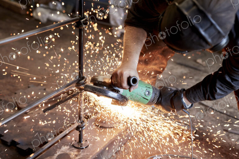An artisan metalworker at work holding an angle grinder, workng on a metal fence.