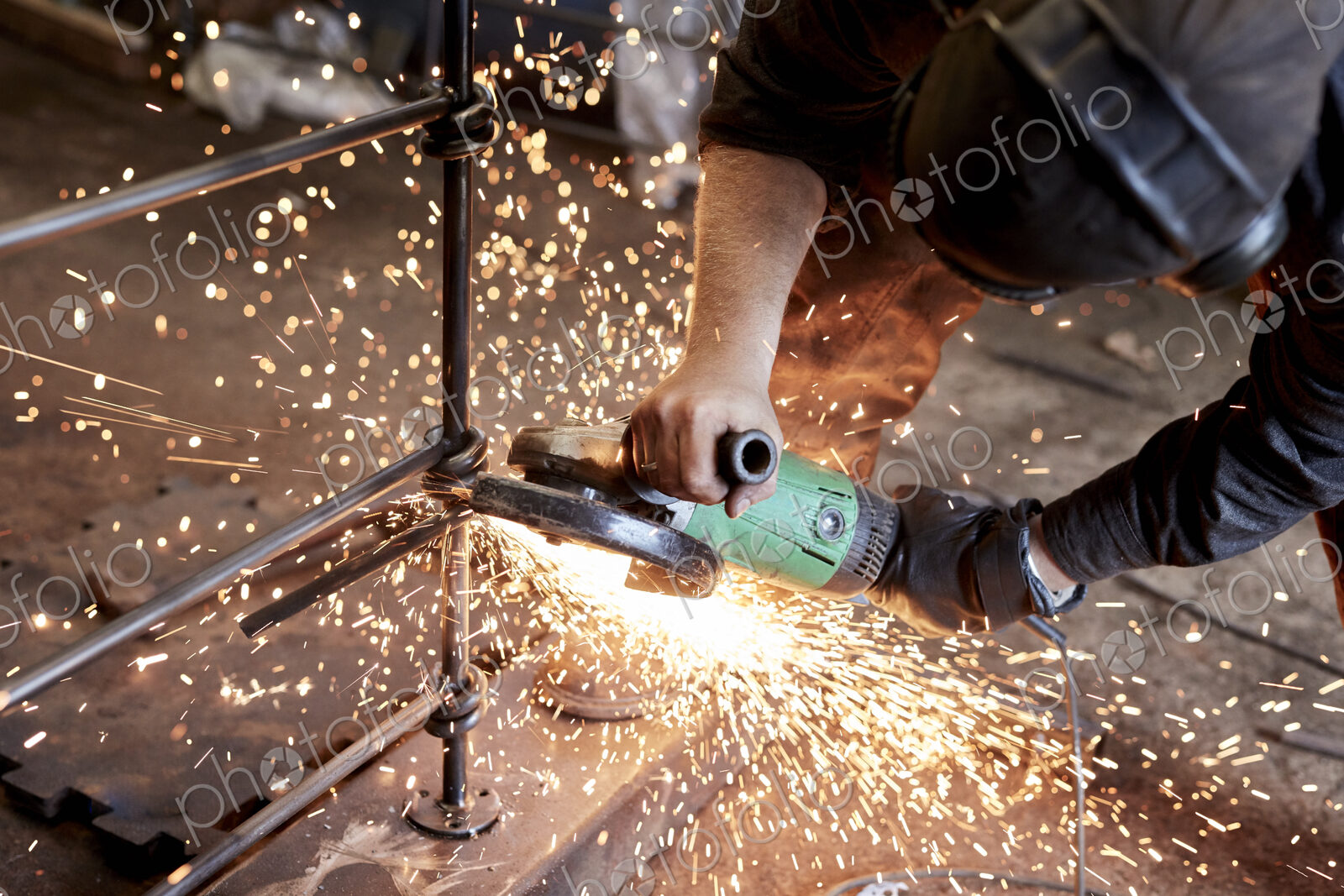An artisan metalworker at work holding an angle grinder, workng on a metal fence.
