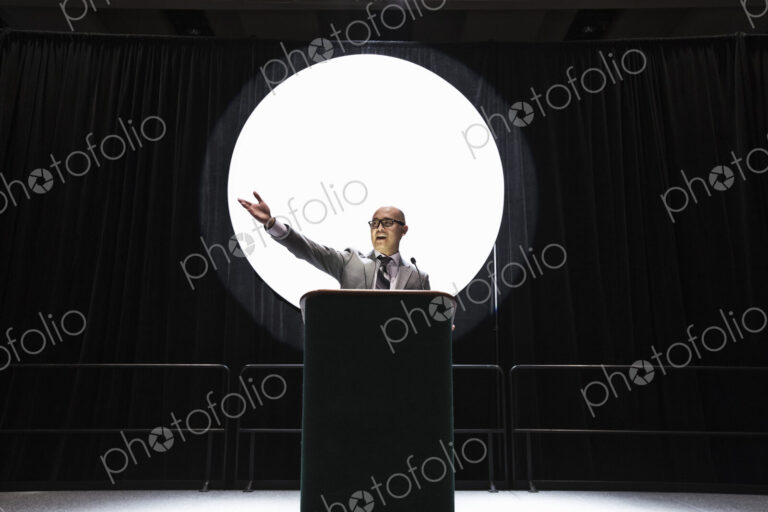 An asian businesman standing at a podium giving a talk at a convention.
