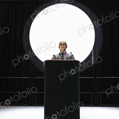 An asian businesman standing at a podium giving a talk at a convention. An asian businesman standing at a podium giving a talk at a convention.