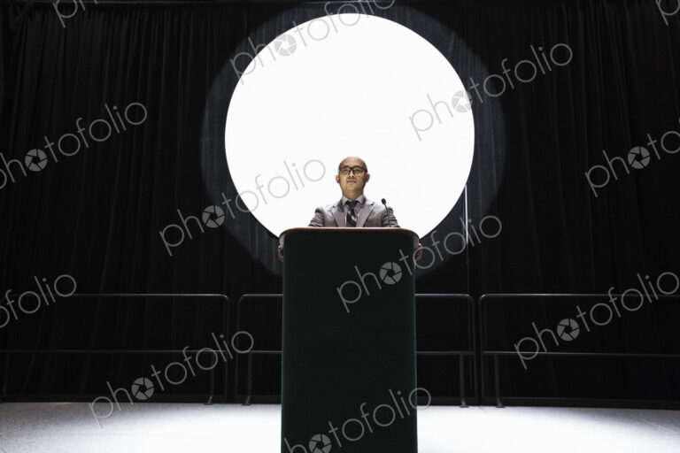 An asian businesman standing at a podium giving a talk at a convention.