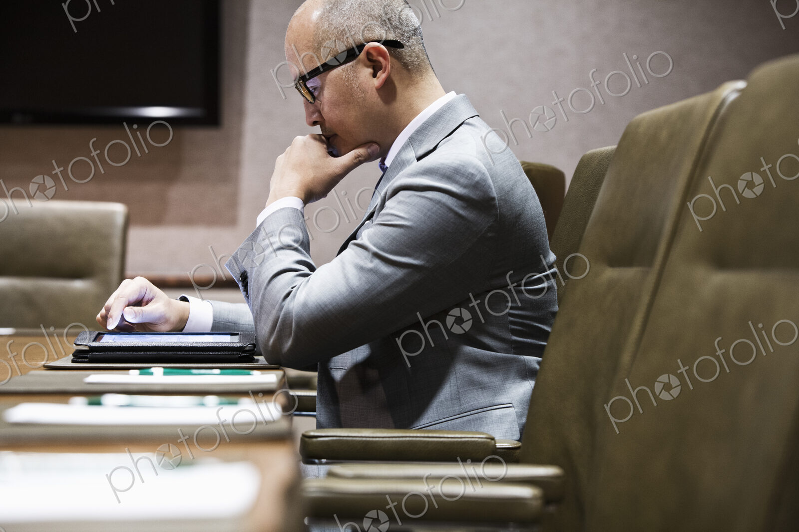 An asian businessman sitting at a conference table working on a notebook computer,…
