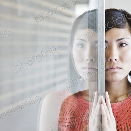 An asian businesswoman reflected on a glass wall in an office lobby. An asian businesswoman reflected on a glass wall in an office lobby.