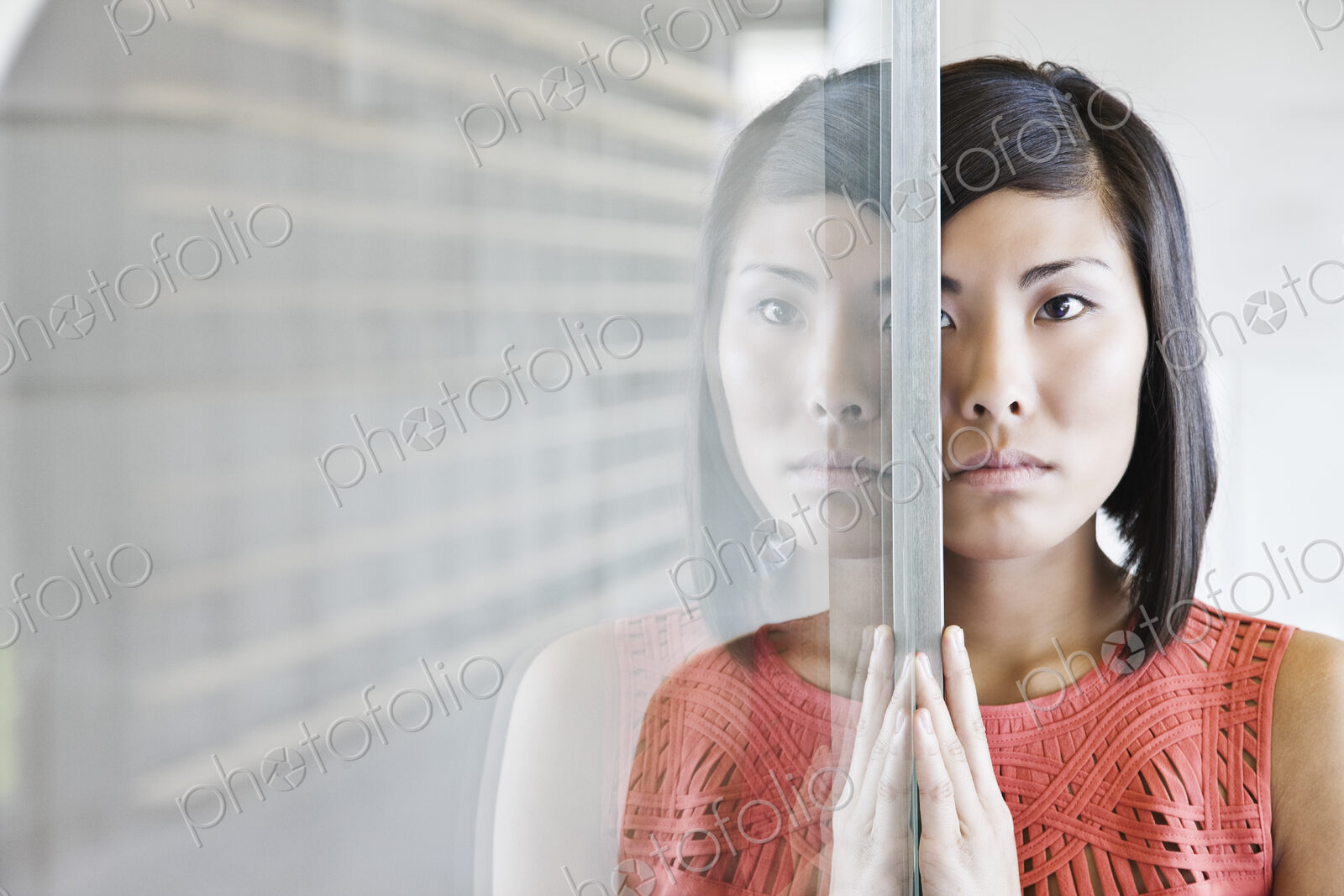 An asian businesswoman reflected on a glass wall in an office lobby.