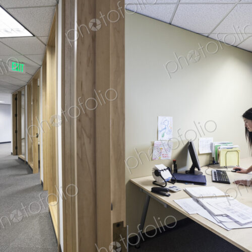 An asian businesswoman working alone in her office next to a long hallway.