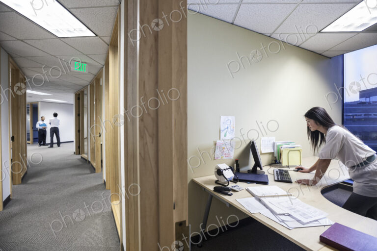 An asian businesswoman working alone in her office next to a long hallway.