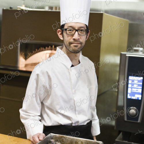 An asian chef working with a roasting pan of mushrooms in a commercial kitchen. An asian chef working with a roasting pan of mushrooms in a commercial kitchen.