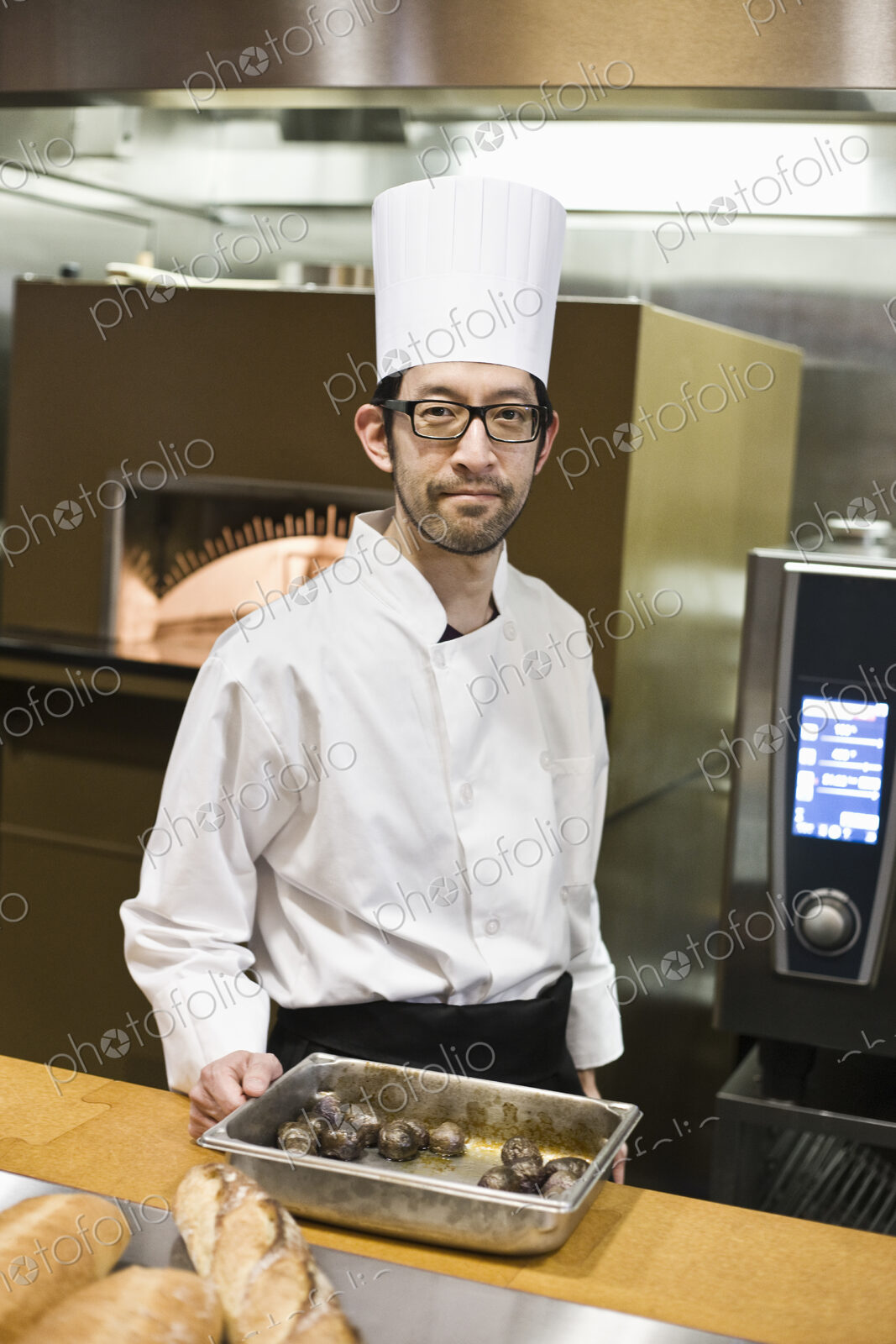 An asian chef working with a roasting pan of mushrooms in a commercial kitchen.