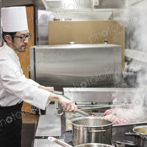 An asian chef working with fresh meat on the grill in a commercial kitchen,