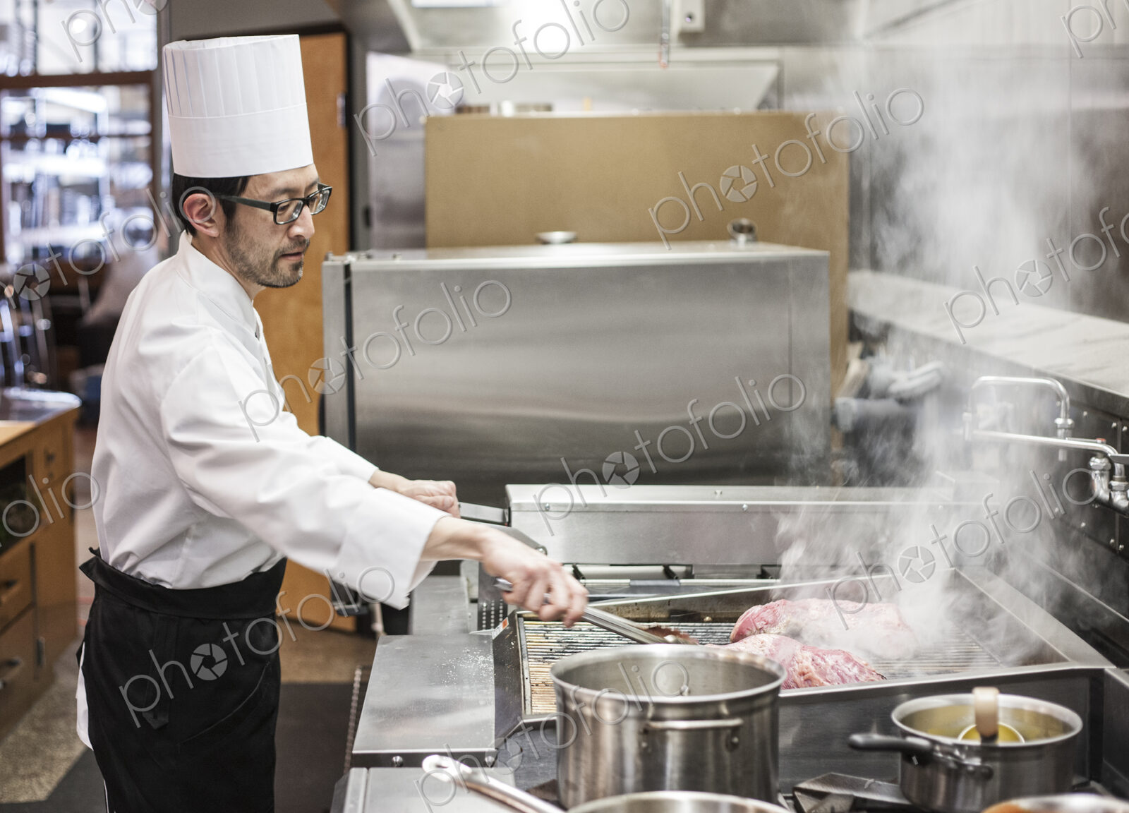 An asian chef working with fresh meat on the grill in a commercial kitchen,