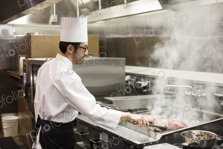 An asian chef working with fresh meat on the grill in a commercial kitchen,