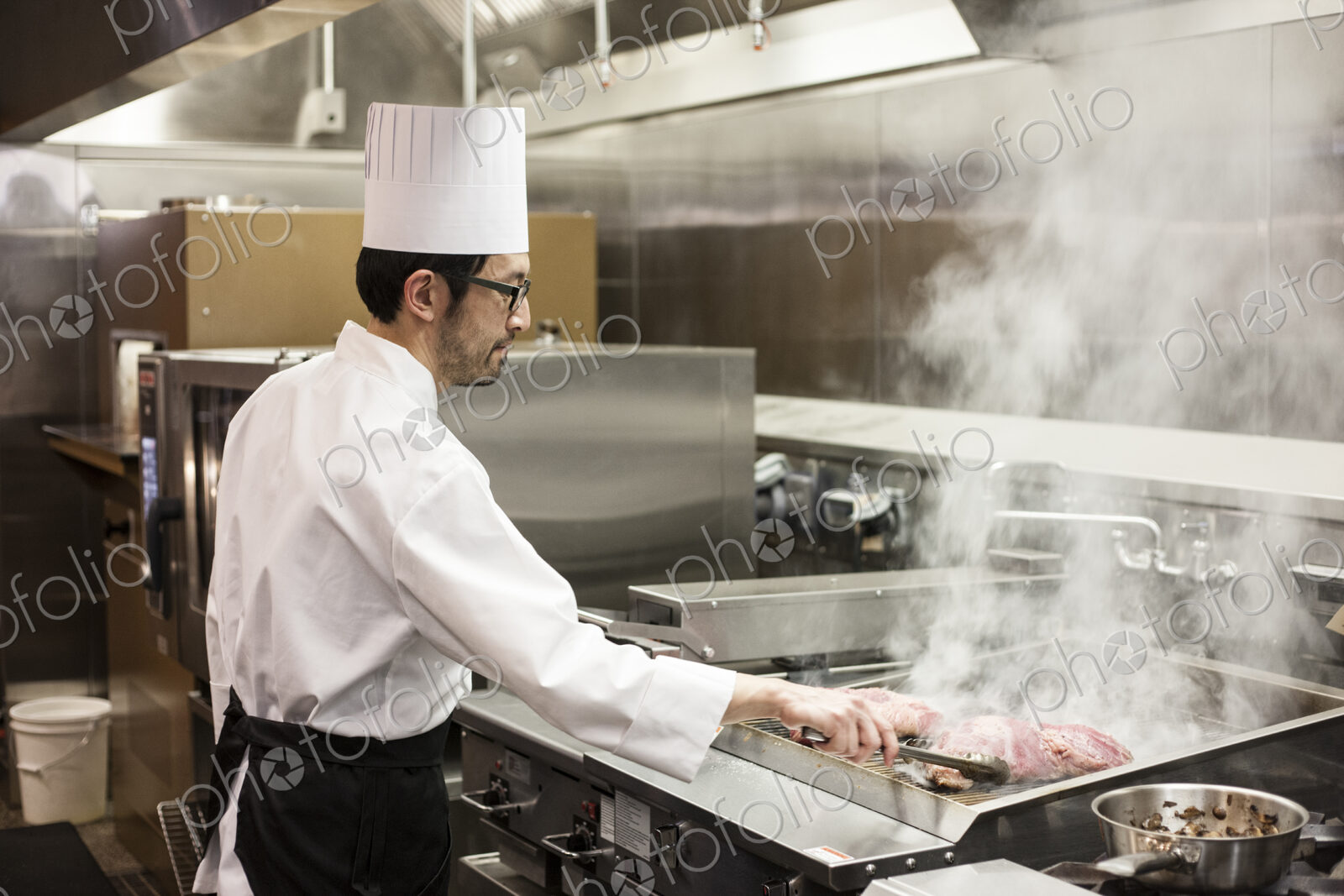 An asian chef working with fresh meat on the grill in a commercial kitchen,