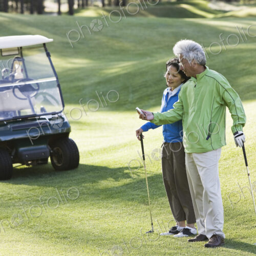 An asian senior couple checking the yards to the flag for the next shot.