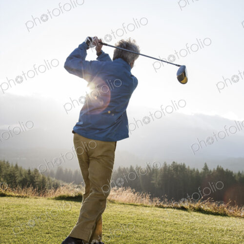 An asian senior man hitting a drive with a golf club.