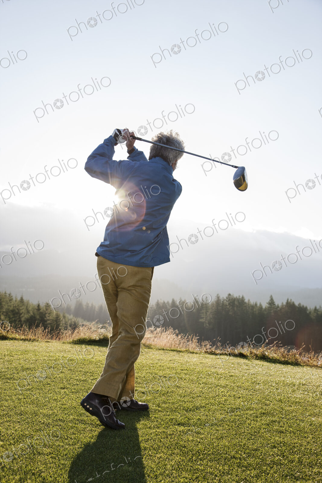 An asian senior man hitting a drive with a golf club.