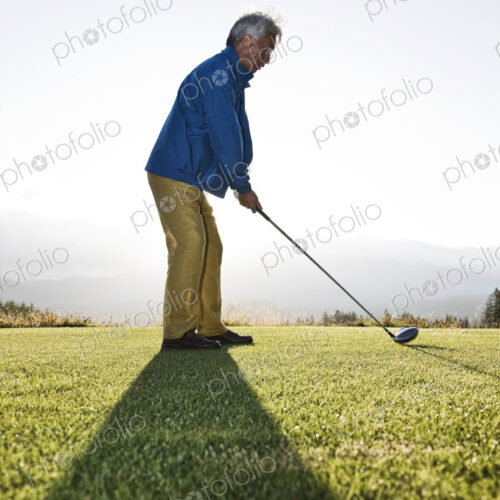 An asian senior man teeing up a golf ball and ready to swing.