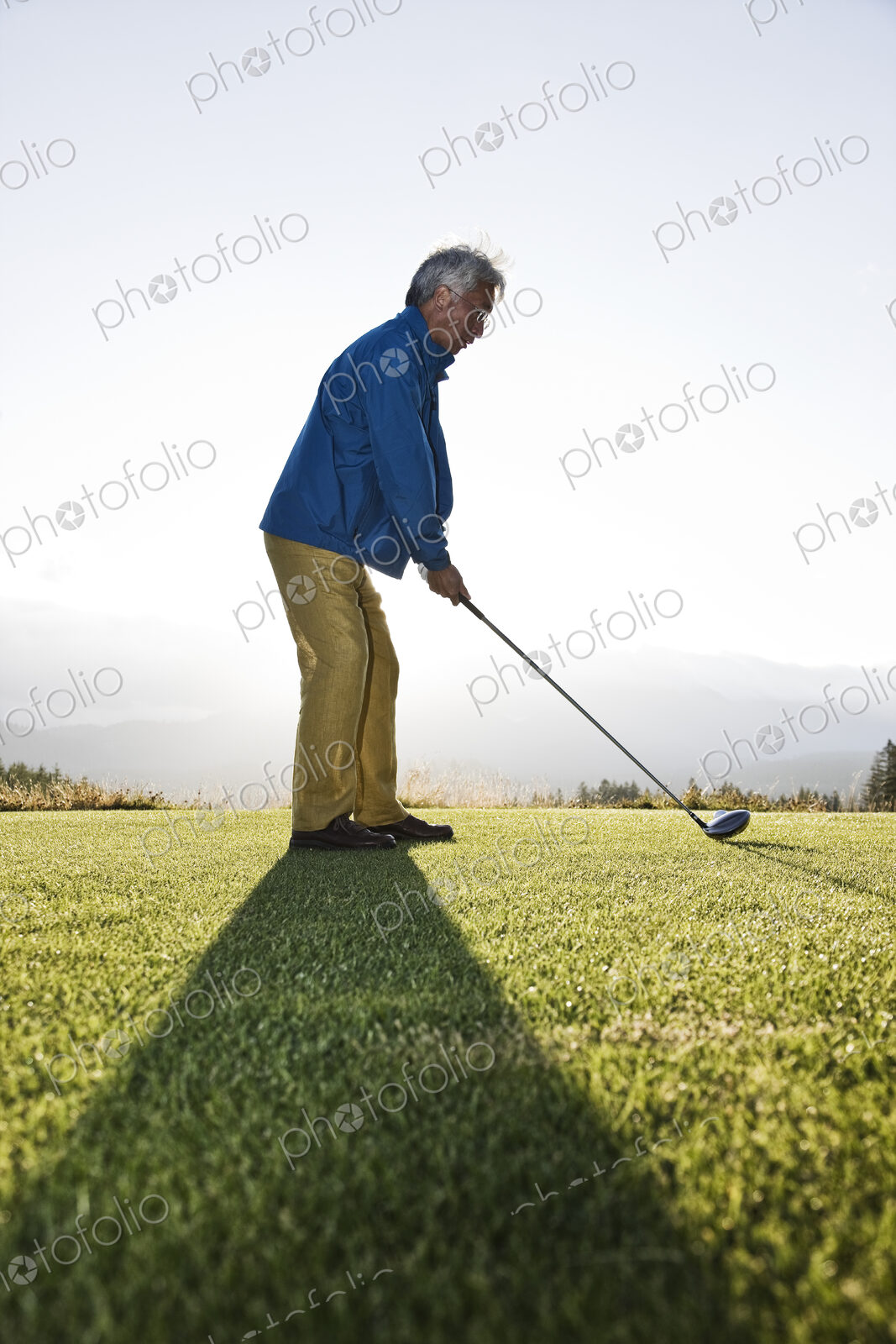 An asian senior man teeing up a golf ball and ready to swing.