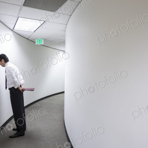 An asisan businessman frustrated and standing with his head against a wall in a hallway. An asisan businessman frustrated and standing with his head against a wall in a hallway.