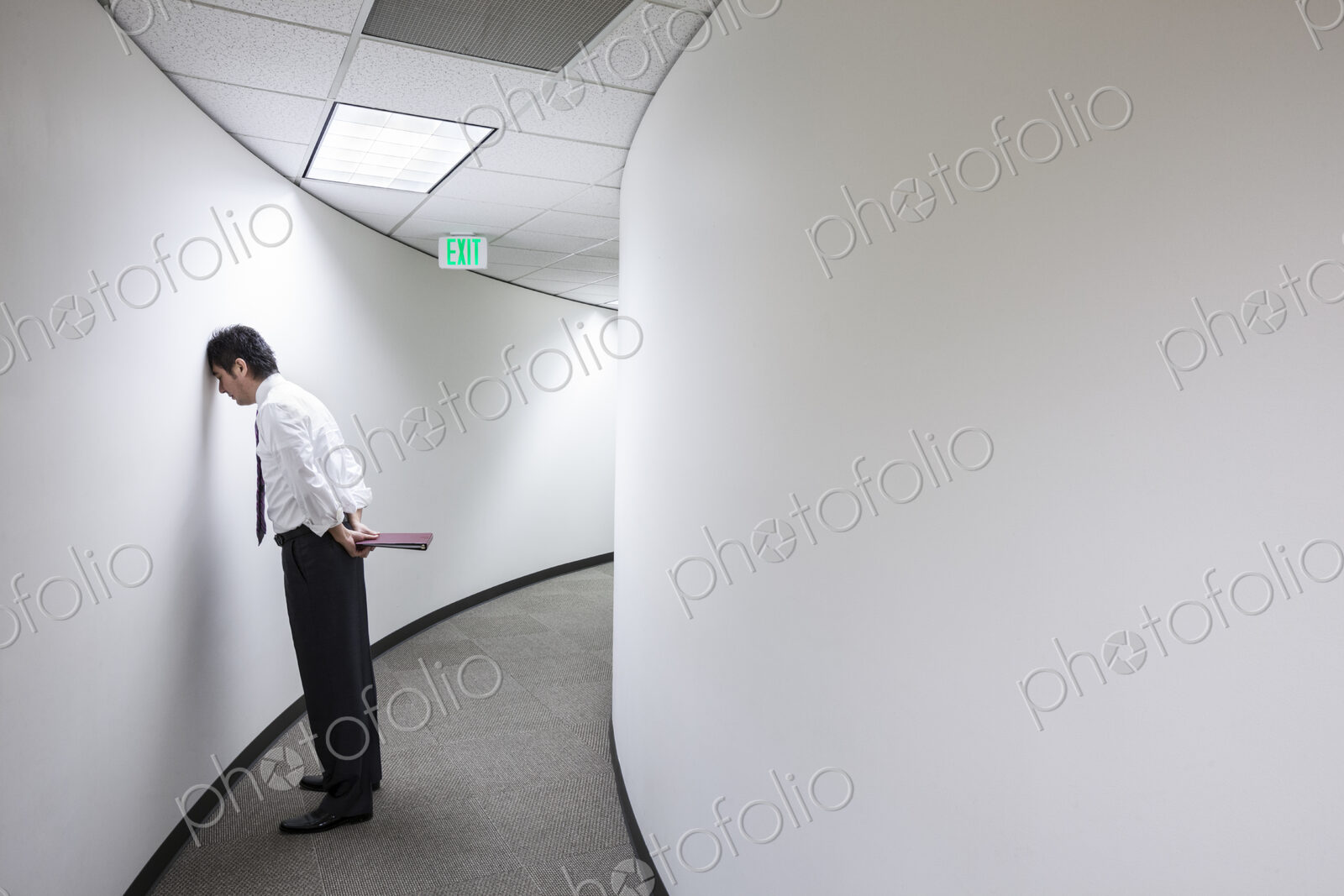 An asisan businessman frustrated and standing with his head against a wall in a hallway.