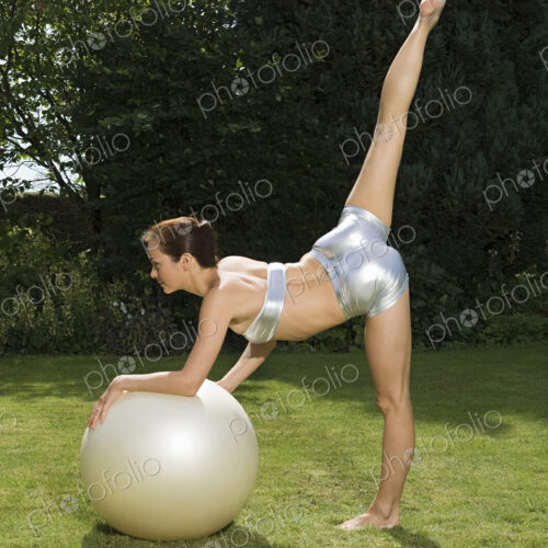 An athlete or gymnast, a young woman leaning on an exercise ball with one leg elevated. An athlete or gymnast, a young woman leaning on an exercise ball with one leg elevated.