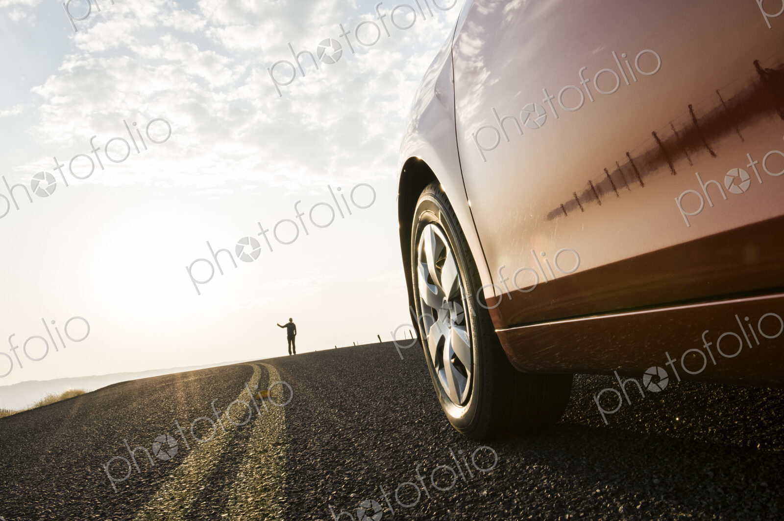 An automobile approaching a person standing on the side of a road.