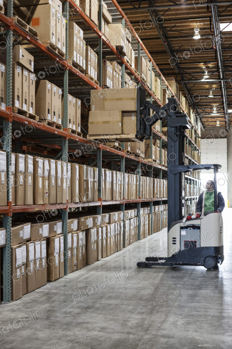 An employee picking products off a rack using a forklift stock picker in a…