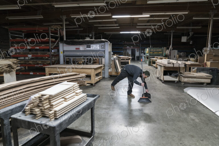 An employee sweeping up after work hours in a large woodworking factory.