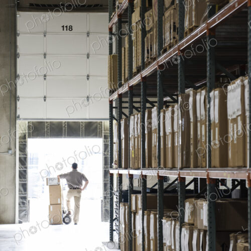 An employee with a hand truck at a loading dock door in a large distribution warehouse. An employee with a hand truck at a loading dock door in a large distribution warehouse.