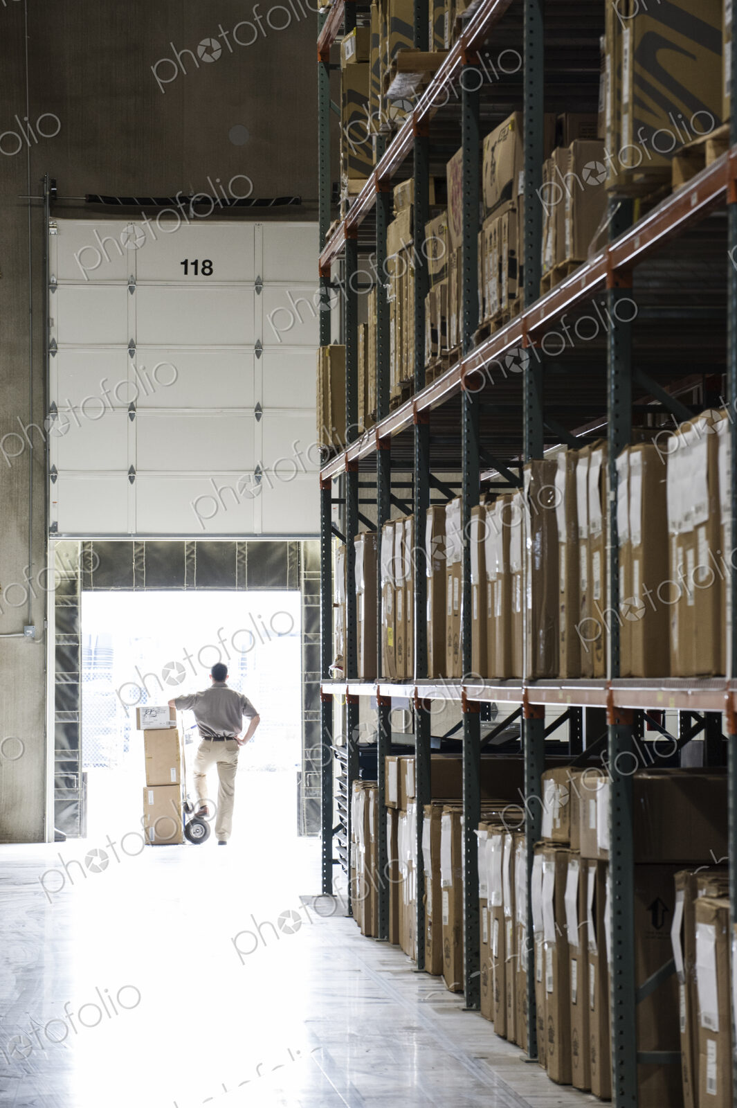 An employee with a hand truck at a loading dock door in a large distribution warehouse.