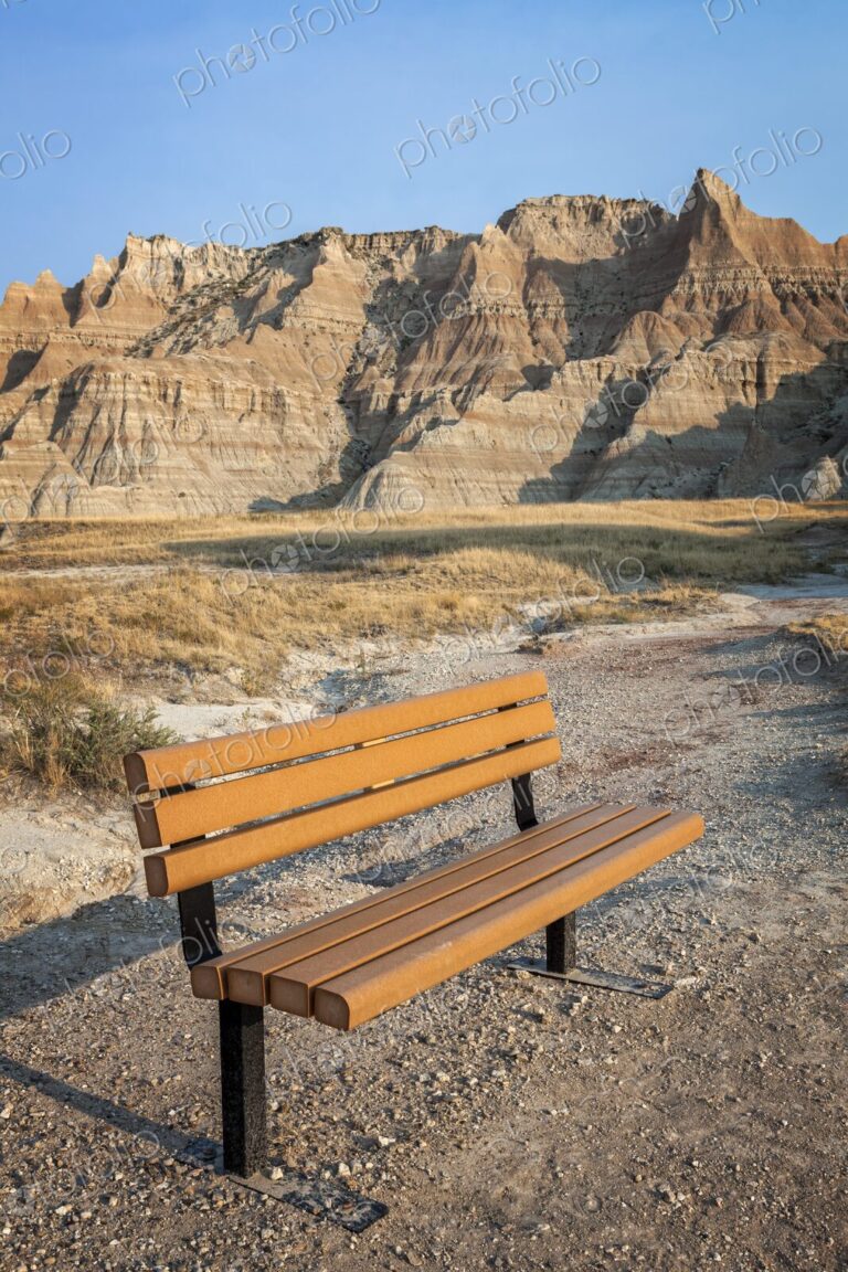 An empty bench faces the layered buttes of Badlands National Park, South Dakota, at…