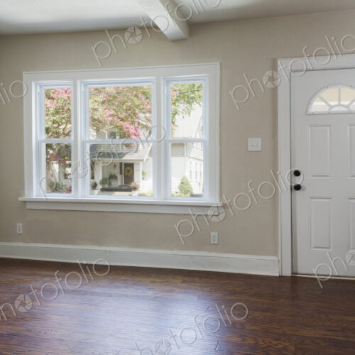 An empty entrance hall with hardwood floors and front door entrance.