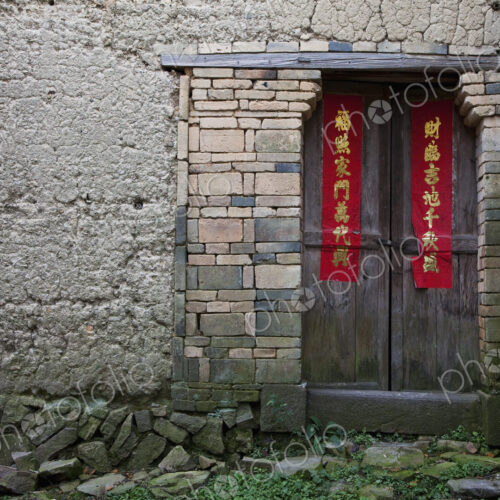 An entrance to a house in an old wall, brickwork and wooden door with red welcome…