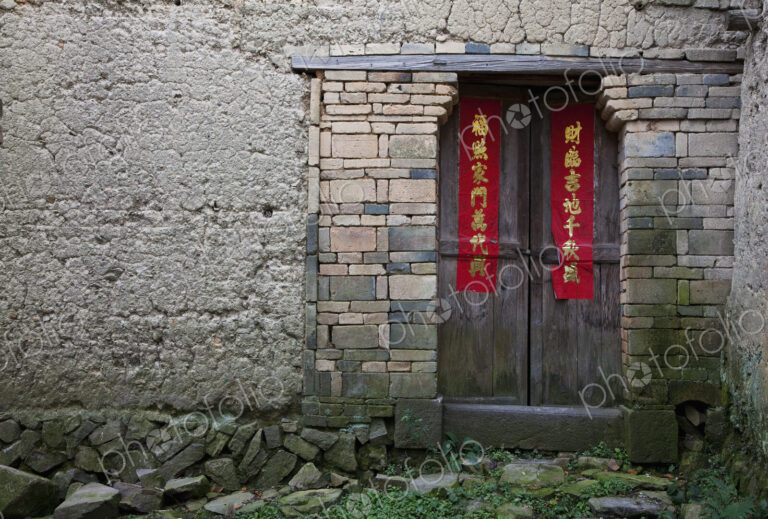An entrance to a house in an old wall, brickwork and wooden door with red welcome…