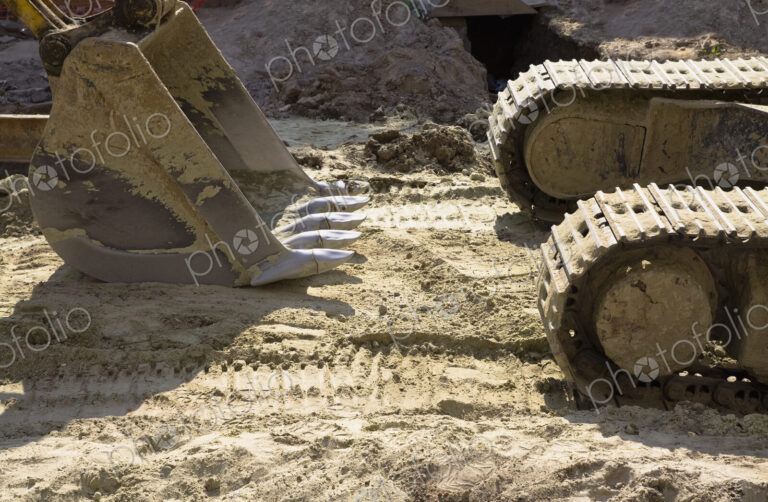 An excavator with caterpillar tracks and a large scoop bucket on a construction site.