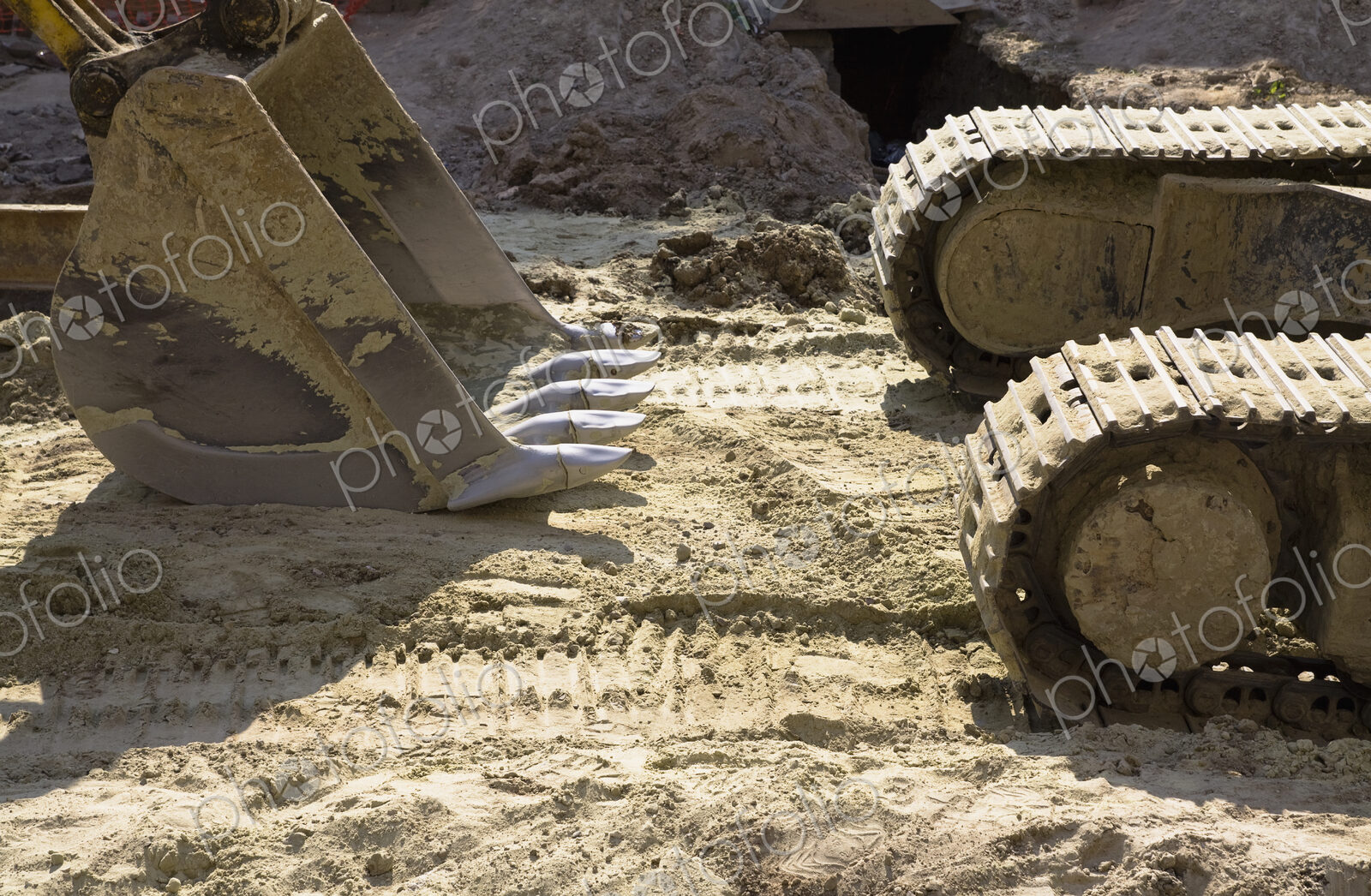 An excavator with caterpillar tracks and a large scoop bucket on a construction site.