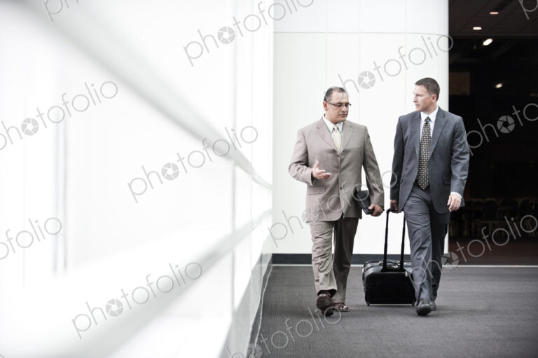 An hispanic businessman and a caucasian businessman walking and talking together in a…