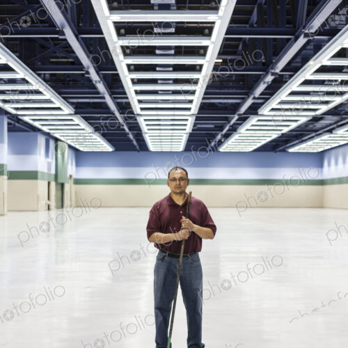An hispanic man standing with a broom in a large convention cener space.