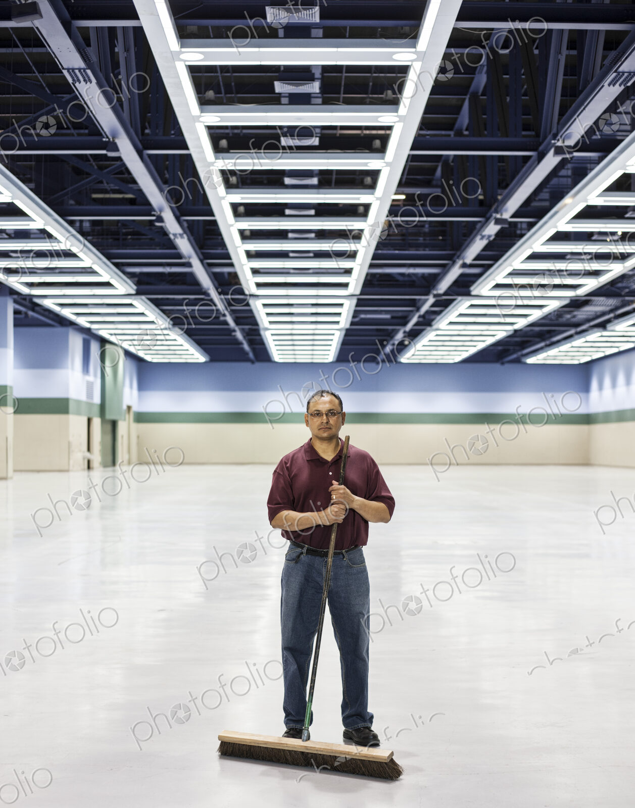 An hispanic man standing with a broom in a large convention cener space.